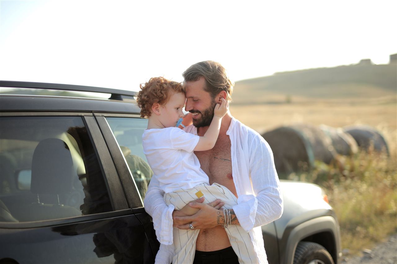 Pai com filho no colo ao lado do carro